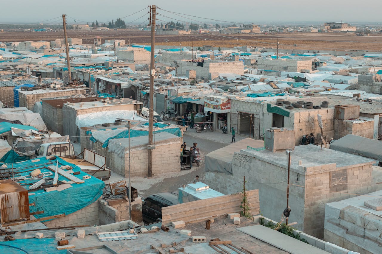 heros-img A broad aerial view of a refugee camp with makeshift shelters and blue tarps in an urban area.