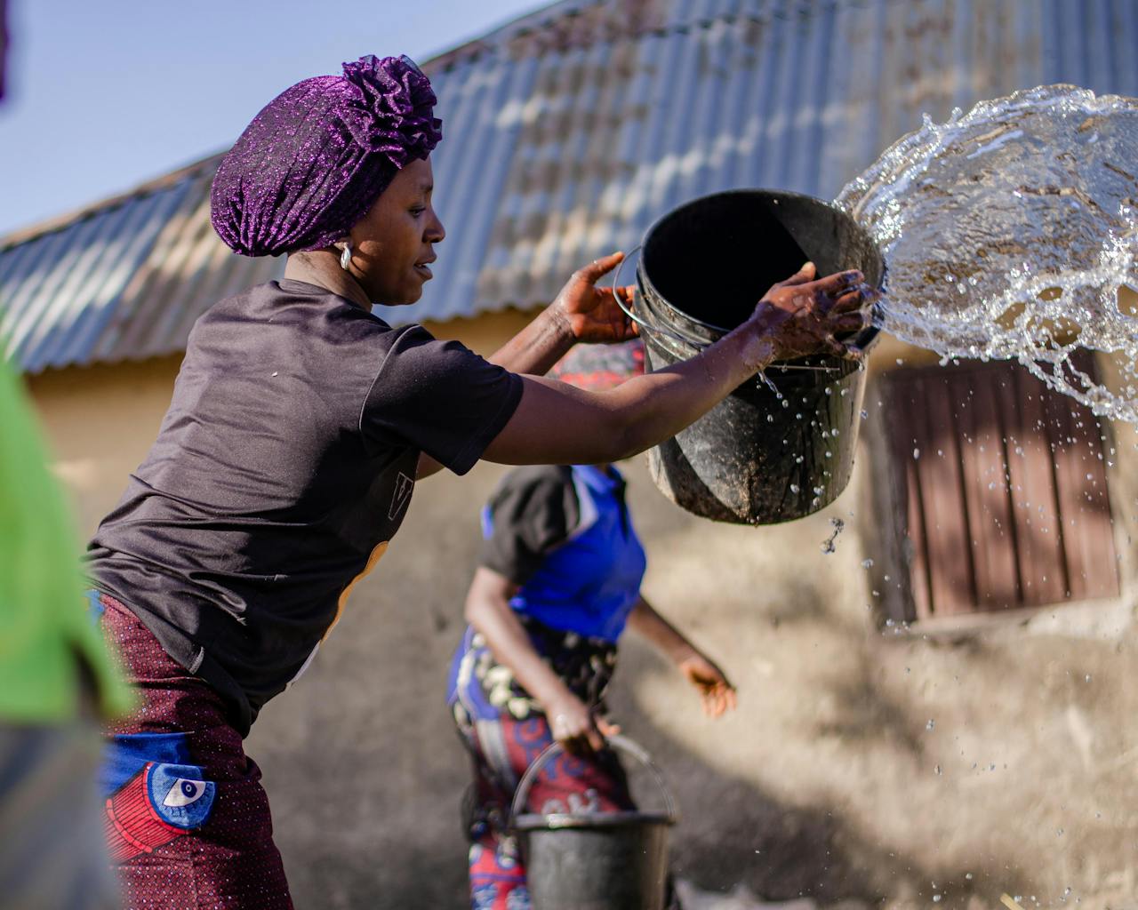 Women engaging in a traditional water activity by a rural home on a sunny day.